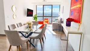 Een moderne eetruimte met een glazen tafel, grijze stoelen en een stadszicht door grote ramen.
