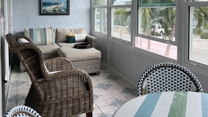 A sunroom with a ceiling fan, wicker furniture, a painting, and large windows offering a view of palm trees and a vehicle. - Lovely renovated condo with water views, great value for outstanding amenities (Clearwater Beach)