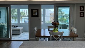 A dining area with a table and chairs, a vase with flowers, and a view through glass doors to the outside. - Lovely renovated condo with water views, great value for outstanding amenities (Clearwater Beach)