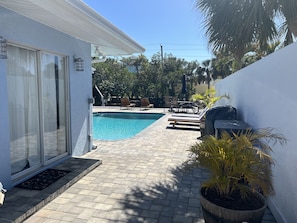Uma área de piscina com piscina azul cristalina, cadeiras de lounge e churrasqueira.