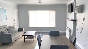 A modern living room with a dining table, sofa, and a large window. - Remodeled rental in the heart of West Hollywood WeHo  (West Hollywood)