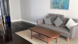 A living room with a grey sofa, two patterned cushions, a wooden coffee table, and a blue painting on the wall. - Remodeled rental in the heart of West Hollywood WeHo  (West Hollywood)
