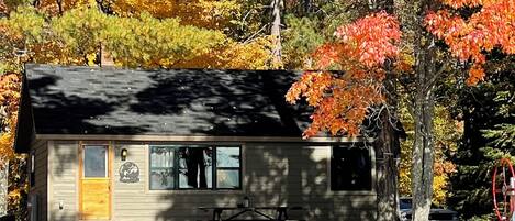 A cabin by a lake with a dock, surrounded by autumn foliage.