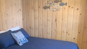 A room with a wooden paneled wall, a bed with a blue bedspread and pillows, and a decorative fish wall art piece. - Cozy Lakefront Cabin Retreat: 3 Bedroom Cabin on South Twin Lake, Conover, WI (Conover)