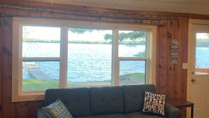 A cozy room with a large window overlooking a body of water, a ceiling fan, and a wooden floor. - Cozy Lakefront Cabin Retreat: 3 Bedroom Cabin on South Twin Lake, Conover, WI (Conover)