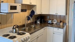 A compact kitchen with white cabinets, a microwave, a kettle, a stove, and a sink. - Cozy Lakefront Cabin Retreat: 3 Bedroom Cabin on South Twin Lake, Conover, WI (Conover)