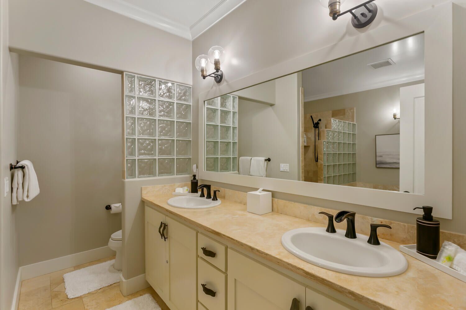 A modern bathroom with two sinks, a large mirror, and frosted glass windows.