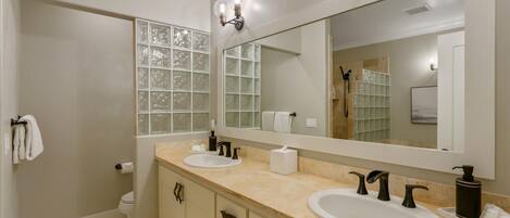 A modern bathroom with two sinks, a large mirror, and frosted glass windows.