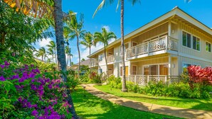 A two-story hotel with a balcony on the second floor, surrounded by lush greenery and palm trees.
