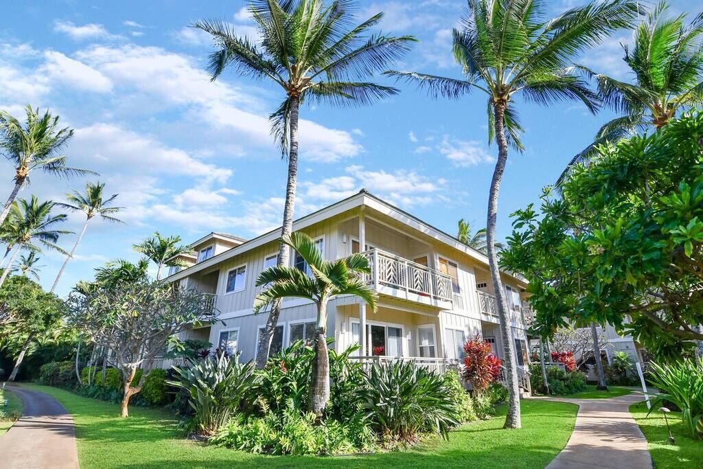 A two-story building with a balcony, surrounded by lush greenery and palm trees.