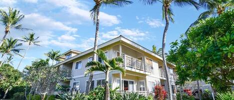 A two-story building with a balcony, surrounded by lush greenery and palm trees.