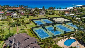 An aerial view of a resort with multiple tennis courts, a swimming pool, and ocean views.