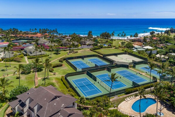 Vista aérea de un resort con varias canchas de tenis, piscina y vistas al océano.