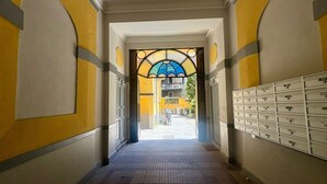 Un pasillo con suelo de baldosas, un ventanal de vidrio azul emplomado y una fila de archivadores blancos a la derecha.