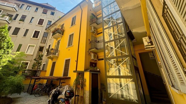 Una estrecha calle urbana con un edificio amarillo que tiene balcones y fachada de vidrio.