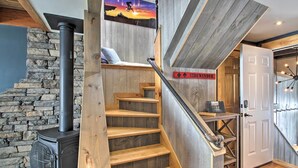 Una escalera con escalones de madera que conduce a una habitación con pared de piedra y estufa de leña.