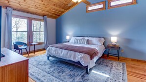 A bedroom with a wooden ceiling, a bed with white bedding, a desk, and a chair. - Honeysuckle Hideaway: Mountain View Leisure Lodge (Ellijay)