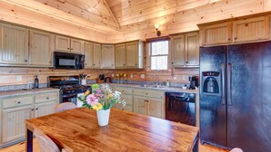 A wooden-paneled kitchen with a wooden dining table, a refrigerator, and a coffee maker. - Honeysuckle Hideaway: Mountain View Leisure Lodge (Ellijay)