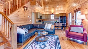 A wooden cabin interior with a living room, kitchen, and staircase. - Honeysuckle Hideaway: Mountain View Leisure Lodge (Ellijay)