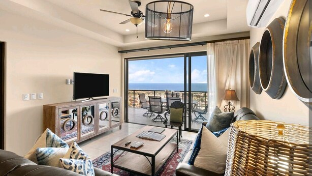 A spacious living room with a large TV, comfortable seating, a coffee table, and a view of the ocean through large sliding doors. - Oceanfront Condo at the Copala (Cabo San Lucas)