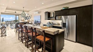 A modern kitchen with a large island, dark cabinetry, stainless steel appliances, and a view of the ocean. - Oceanfront Condo at the Copala (Cabo San Lucas)