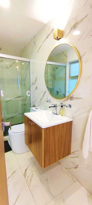 A bathroom with a marble wall, a wooden vanity, a round mirror, and a glass shower enclosure. - Polanco Close to Shopping Malls 3BR 3BT (Ciudad de México)