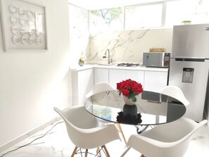 Una cocina moderna con salpicadero de mármol, armarios blancos, horno empotrado y una mesa de comedor de vidrio con dos sillas.