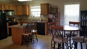 Una cocina con armarios de madera, un refrigerador negro, un lavavajillas y un comedor con una mesa redonda y sillas.