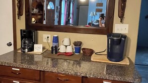 A kitchen with a marble countertop, a coffee maker, a kettle, and a sink.