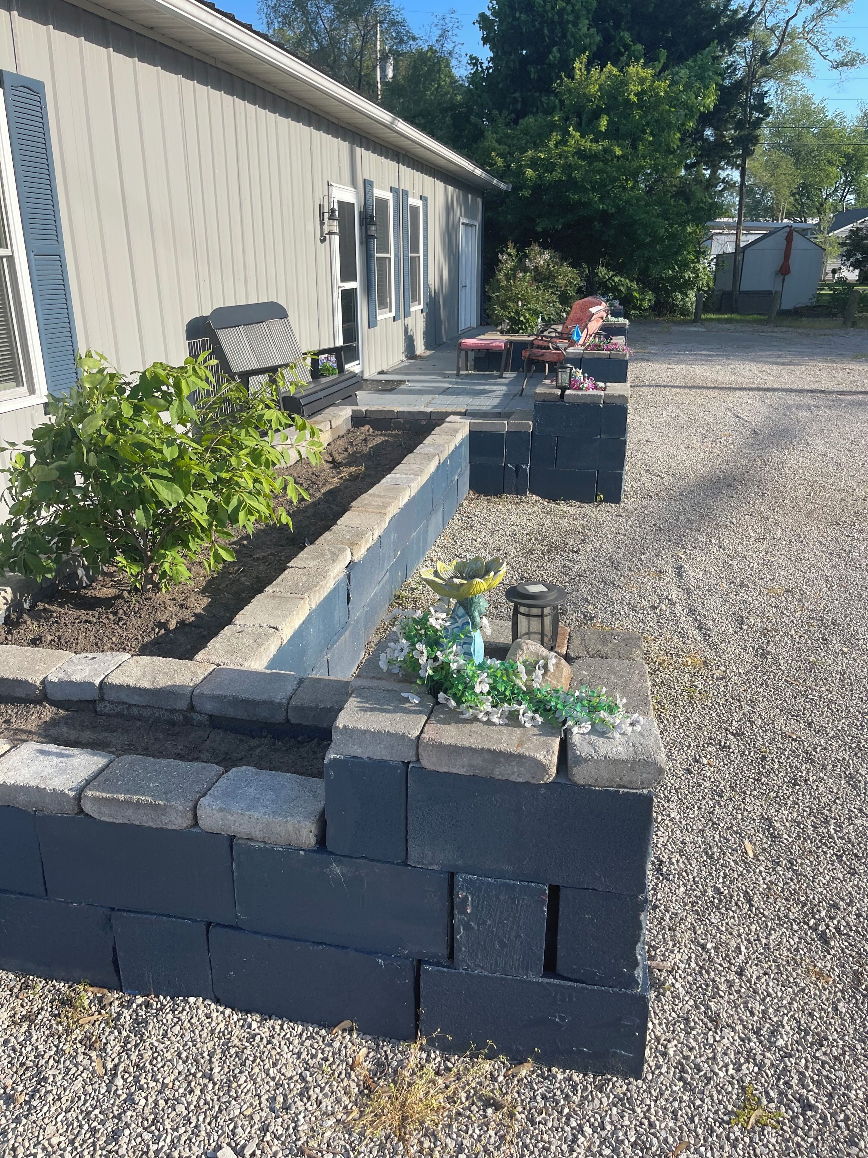 Un immeuble résidentiel avec une allée en gravier, un parterre surélevé planté de végétaux et du mobilier d’extérieur.