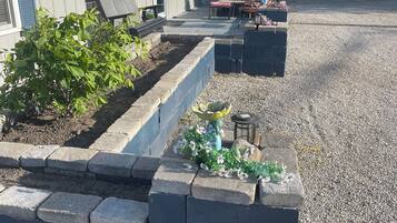 Un immeuble résidentiel avec une allée en gravier, un parterre surélevé planté de végétaux et du mobilier d’extérieur.