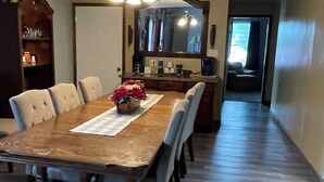 A dining area with a long wooden table, six chairs, a chandelier, a mirror, and a wooden cabinet.