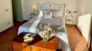 Een slaapkamer met een houten plafond, een bed met een beddekleed met dessin, een nachtkastje met een bloevas en een houten nachtkastje.