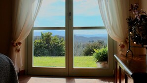 Een kamer met een schuifdeur die leidt naar een balkon met uitzicht op groen en bergen.