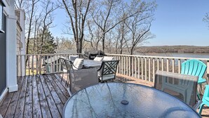 Une terrasse en bois, aménagée avec du mobilier d’extérieur, notamment une table et des chaises, qui offre une vue sur une étendue d’eau et des arbres.