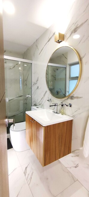 A modern bathroom with a marble vanity, a round mirror, and a glass shower enclosure.