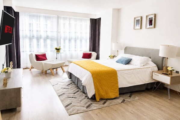 A modern hotel room with a bed, bedside table, lamp, and a TV mounted on the wall.