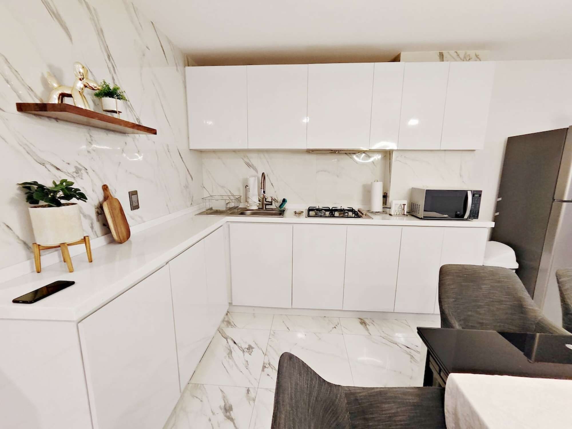 Une cuisine moderne avec des armoires blanches, un comptoir en marbre, une cuisinière à gaz, un four à micro-ondes et un réfrigérateur.