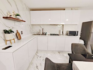 Una cocina moderna con armarios blancos, encimera de mármol, estufa a gas, microondas y refrigerador.