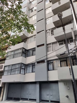 A multi-story residential building with a modern architectural design, featuring balconies, large windows, and a visible garage entrance.