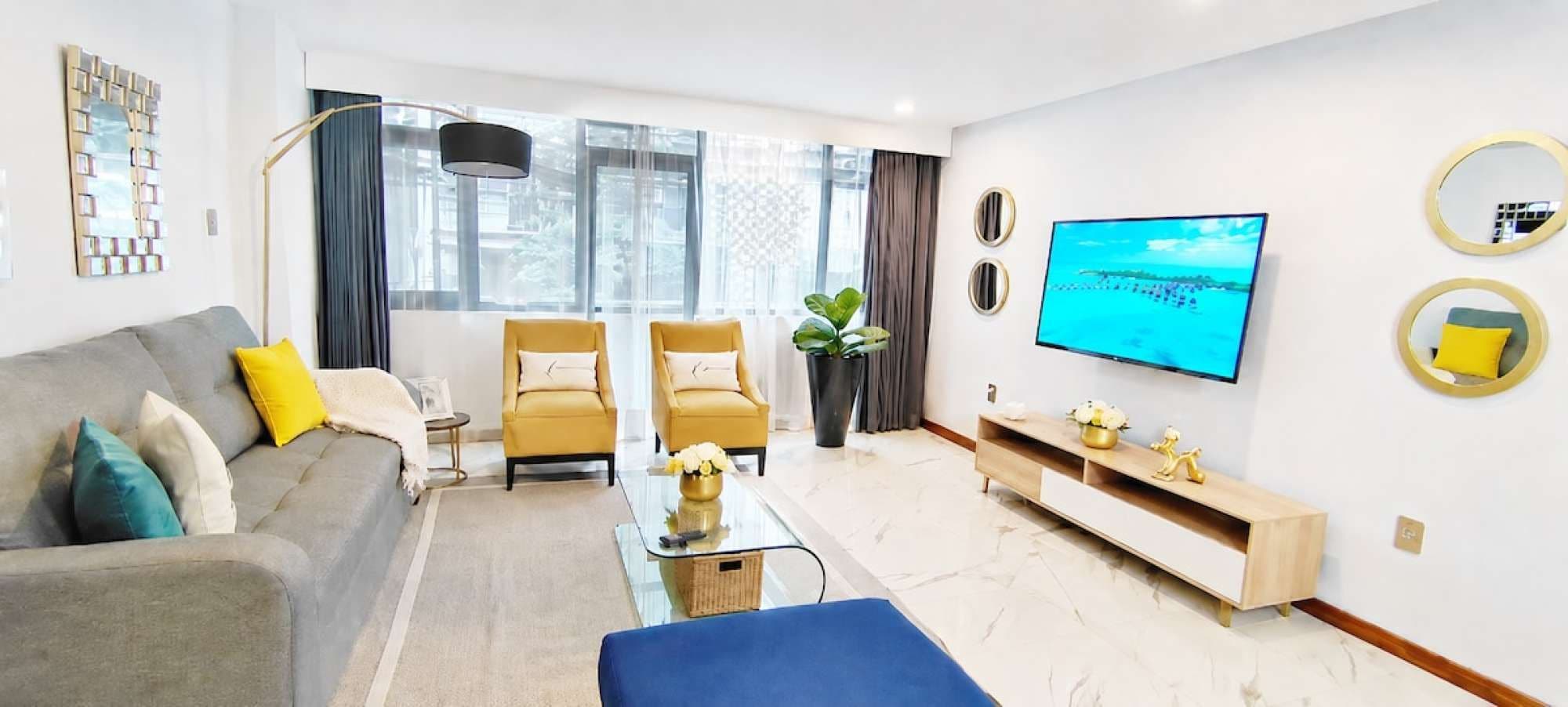 A modern living room with a sofa, two armchairs, a coffee table, a TV, and a console table with decorative items.