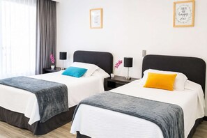 A hotel room with two beds, each with a black headboard, white bedding, and a single bedside table with a lamp.