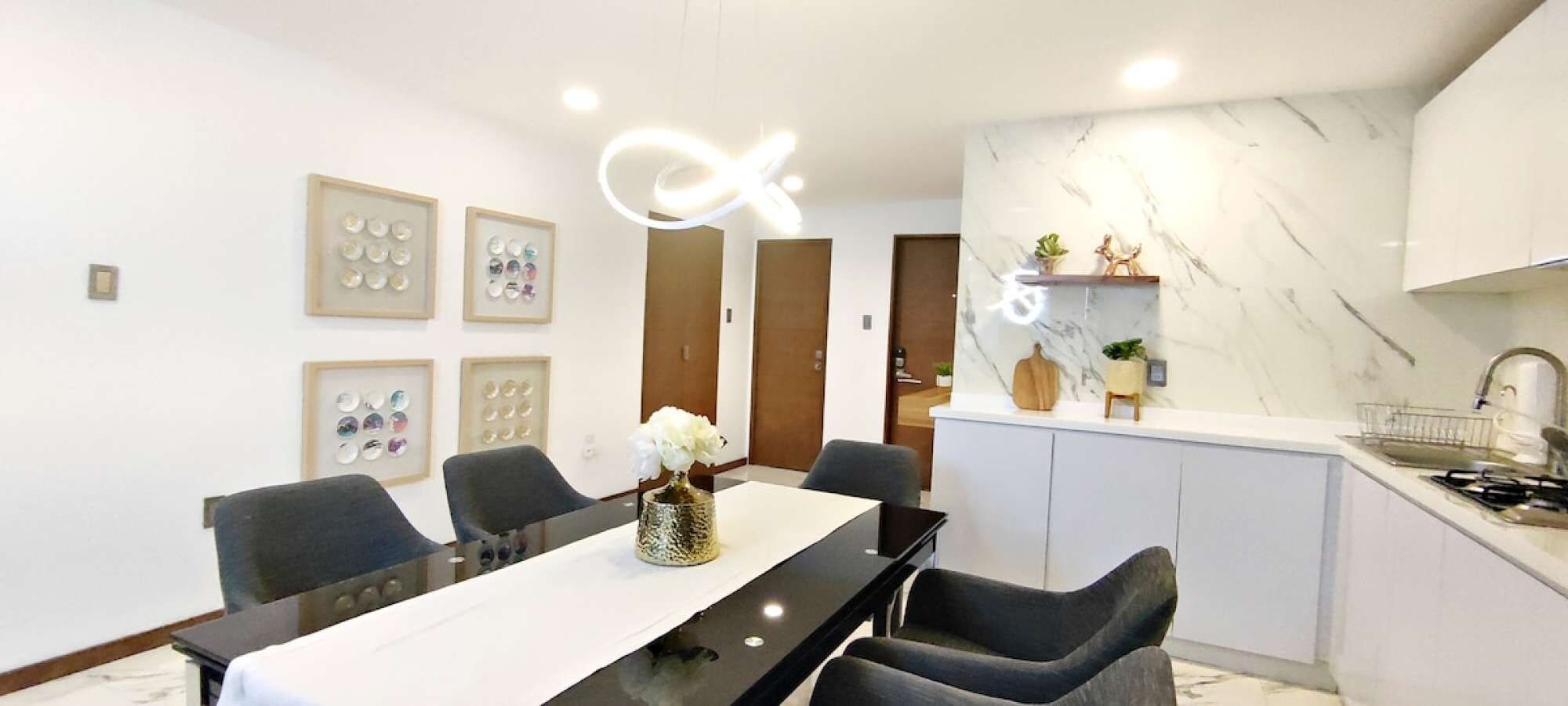 Une cuisine moderne avec un plan de travail en marbre, un coin repas avec une table et des chaises noires, et des tableaux encadrés accrochés au mur.
