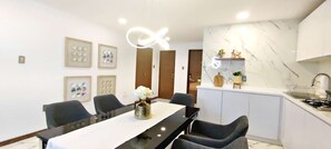 Una cocina moderna con encimera de mármol, un comedor con mesa y sillas negras, y cuadros en la pared.
