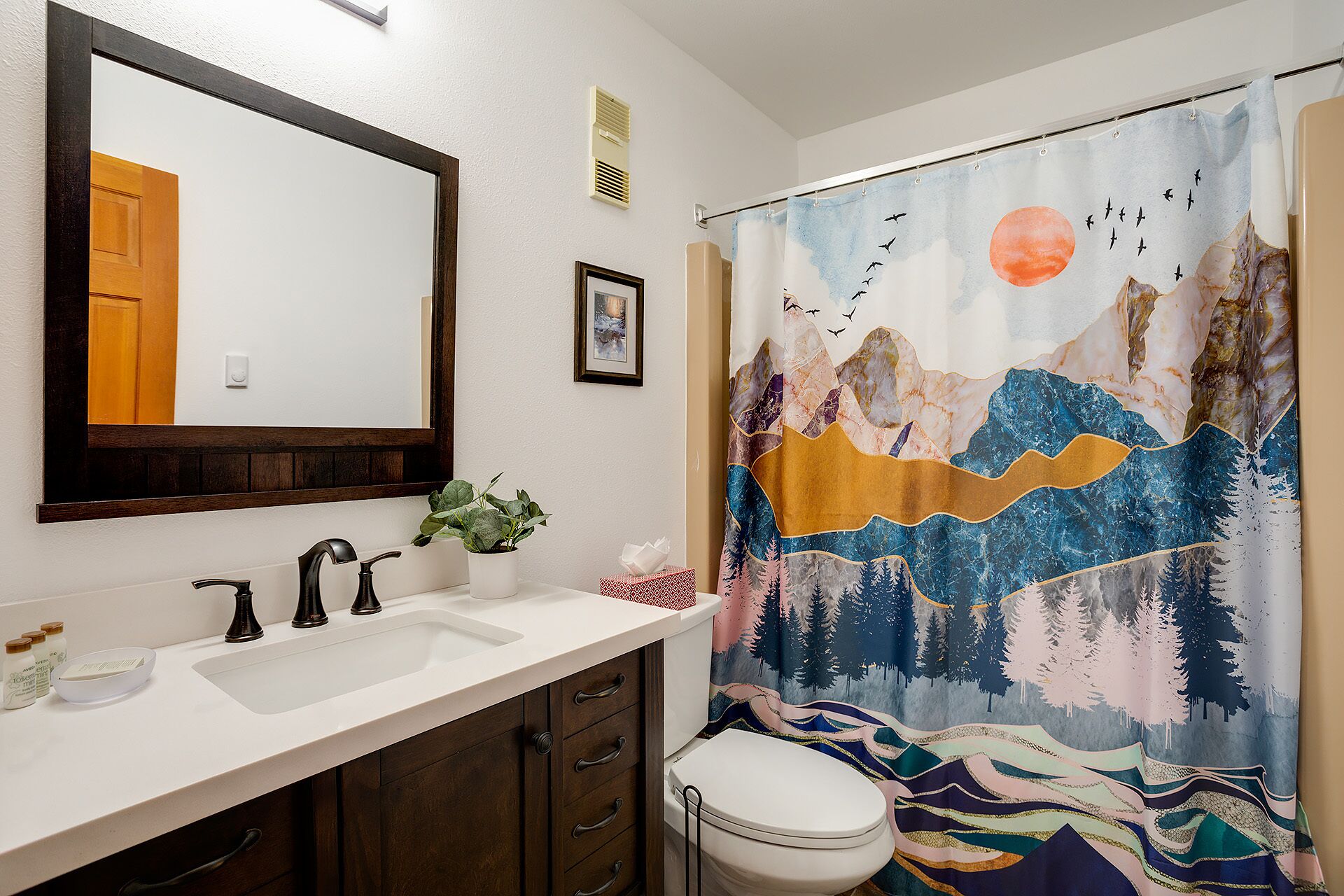 A bathroom with a white sink, dark wooden cabinets, a mirror, and a shower curtain with a mountain and bird design.