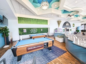 Uma mesa de bilhar em ambiente interno moderno, com parede verde e área de bar.