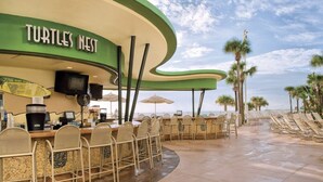 A beachside bar named 'Turtles Nest' with outdoor seating and palm trees in the background.