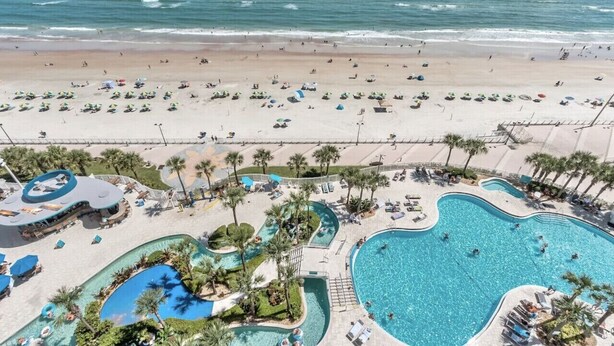 A resort with a large beach, multiple swimming pools, and palm trees.