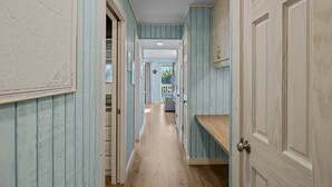 Passadís estret amb parets de blau clar i terres de fusta que condueix a una habitació amb una finestra i una porta.