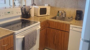 Una cocina compacta con armarios de madera, un microondas, una estufa, un lavabo y un lavavajillas.